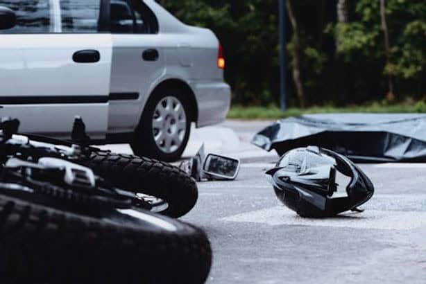 Close-up of a street accident involving a motorcycle and a car. A helmet and motorcycle lie on the ground near the car.