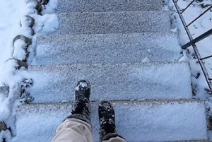 Person wearing boots walking down snowy steps outdoors.