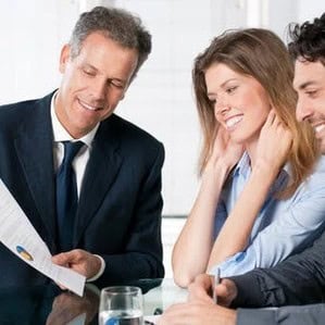 Three people in business attire sitting at a table, reviewing a document.