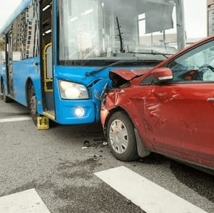 A blue bus and a red car have collided at an intersection, with the car's front crumpled against the bus's side. Debris is scattered on the road.