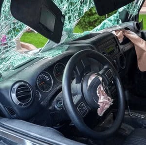 Car interior showing a shattered windshield and deployed airbags.