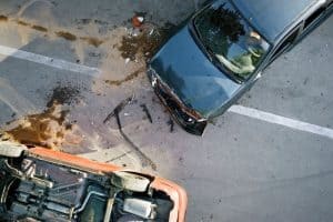 Overhead view of two cars involved in an accident on a road, one flipped over with visible damage and debris scattered around them.