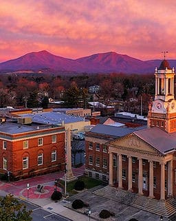 Aerial view of a small town at sunset, featuring a courthouse with a clock tower and mountains in the background under a pink sky.