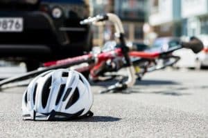 White helmet on the ground in front of a fallen bicycle and a car in the background on a city street.