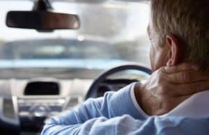 Man in a car touching the back of his neck, looking toward the windshield.
