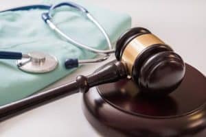 A judge's gavel on a wooden base is placed next to a folded medical gown and a stethoscope.