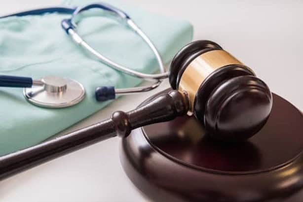 A judge's gavel on a wooden base is placed next to a folded medical gown and a stethoscope.