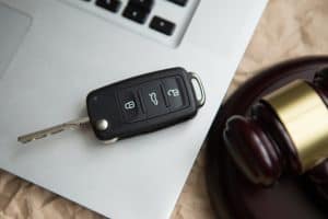 A car key fob lies on a partially visible laptop keyboard next to a wooden gavel on a light brown surface.