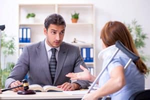 Man in a suit listens attentively to a woman with a neck brace and crutches in an office setting.