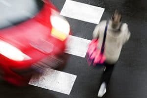 Blurred red car and person with a pink bag crossing a street at a crosswalk.