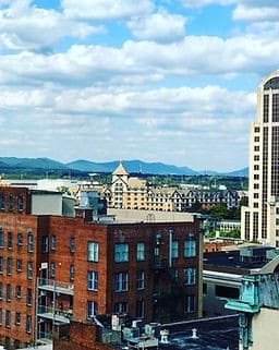 View of city buildings with mountains in the background under a partly cloudy sky.