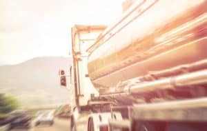 A tanker truck drives on a highway with blurred motion, surrounded by other vehicles and mountains in the background.