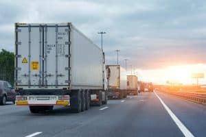 Trucks driving on a highway at sunset, with a clear sky and visible road signs.
