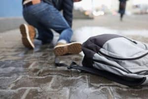 Person kneeling on wet pavement with a gray and black backpack on the ground nearby.