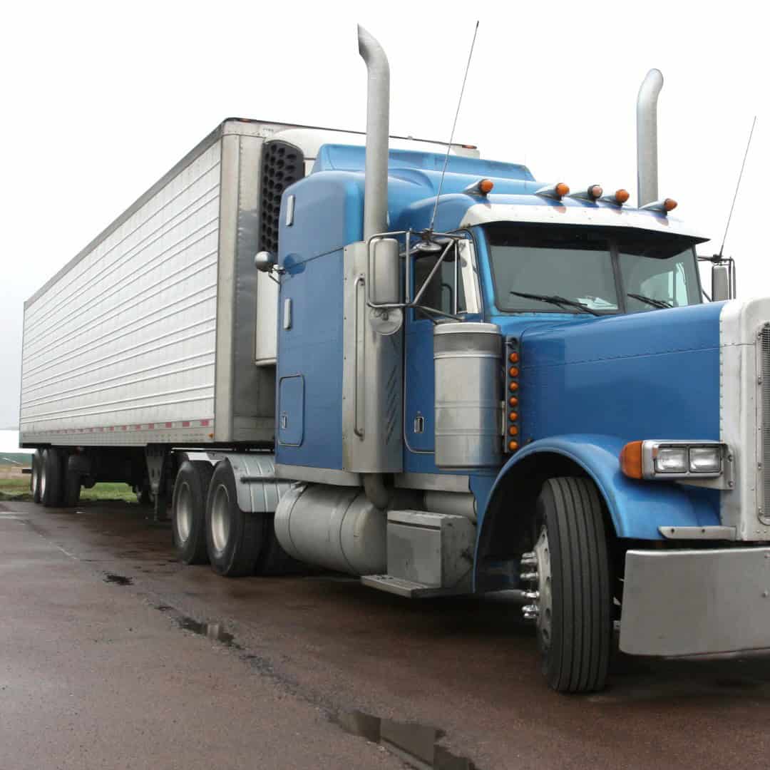 A large blue semi-truck with a silver trailer is parked on a wet road.