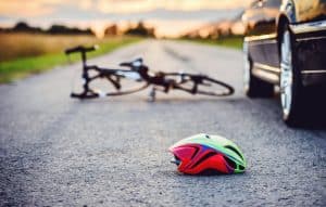 A bicycle and a helmet are on the road beside a car during sunset.