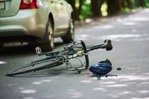 A fallen bicycle and helmet lie on the road near a car.