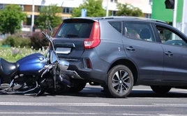A motorcycle is wedged under the rear of a gray SUV in a collision on a street.