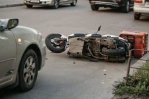 A motorcycle lies on its side on the street near parked cars, indicating a traffic incident.