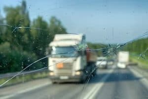 Cracked windshield with blurred view of trucks on a highway in the background.