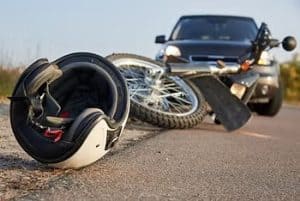 Helmet and motorcycle lying on the road in front of a car, suggesting a collision.
