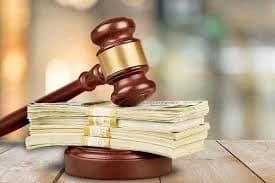 A judge's gavel rests on stacks of money on a wooden surface, symbolizing legal and financial matters.
