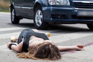 A person lies face down on a crosswalk in front of a car, suggesting a possible accident or emergency situation.