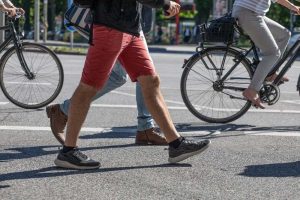 People walking and cycling in a city street intersection on a sunny day.