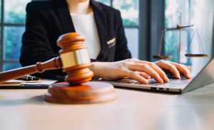 A person typing on a laptop near a gavel and scales of justice, symbolizing legal work.