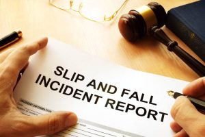 A person holds a "Slip and Fall Incident Report" form on a desk with a gavel, legal book, and glasses.