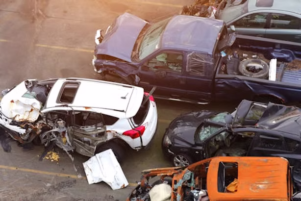 Several heavily damaged vehicles, including cars, a truck, and an SUV, are piled close together in what appears to be a junkyard or salvage yard.
