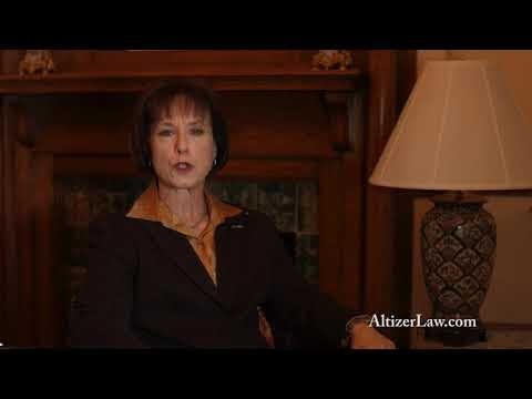 A person in a dark suit sits in a dimly lit room with a fireplace and lamp, speaking to the camera. The text "AltizerLaw.com" is visible.